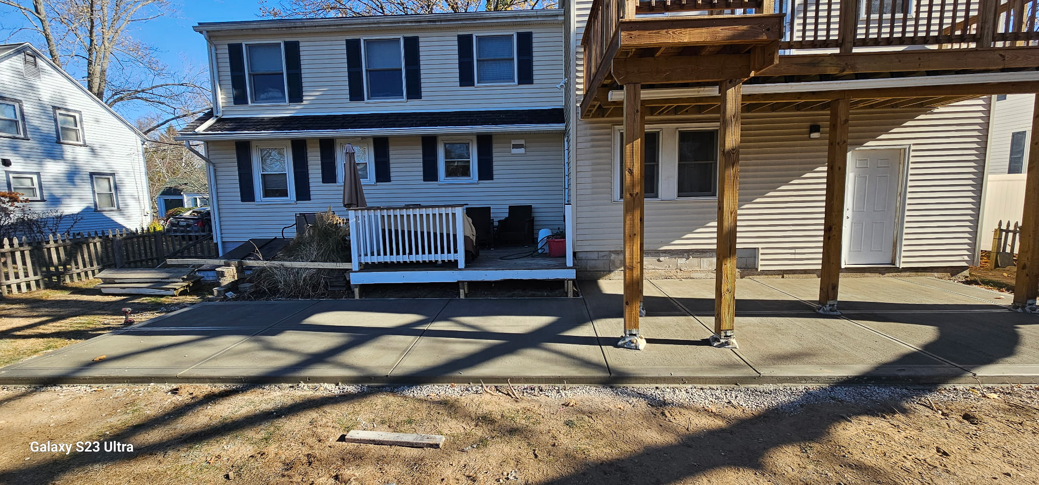 Concrete patio installation beside a raised deck by Patriot Concrete