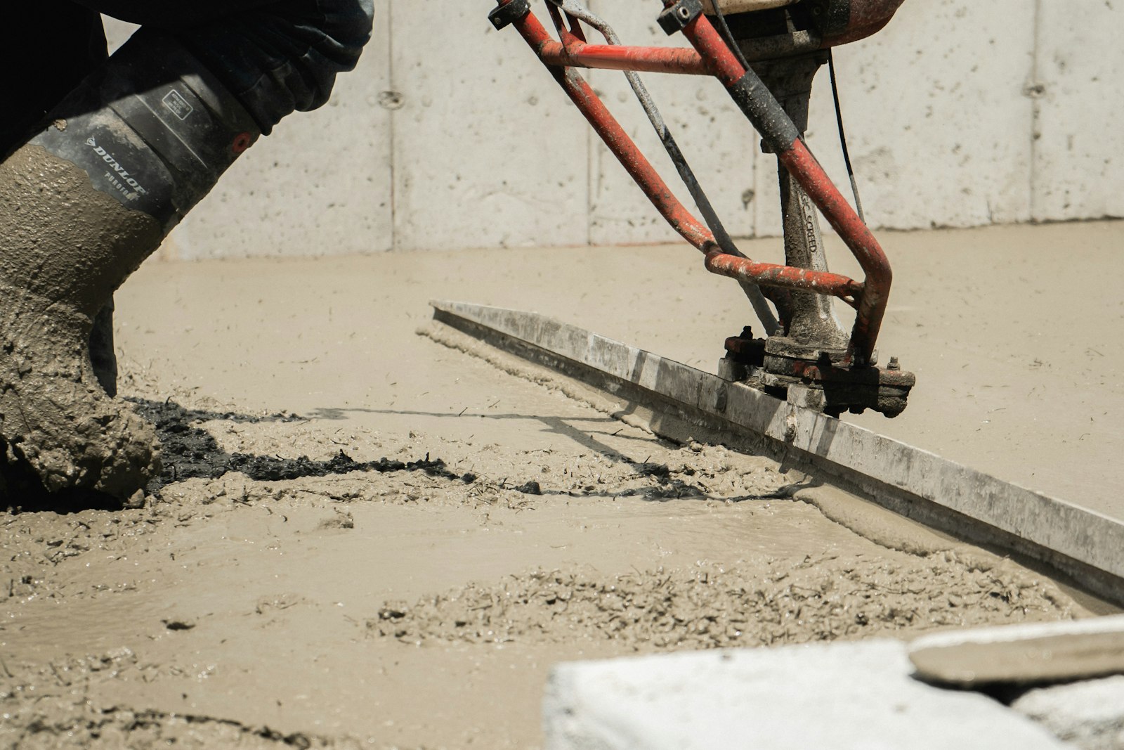 A concrete contractor screeding and leveling fresh concrete flatwork with a power screed along a foundation