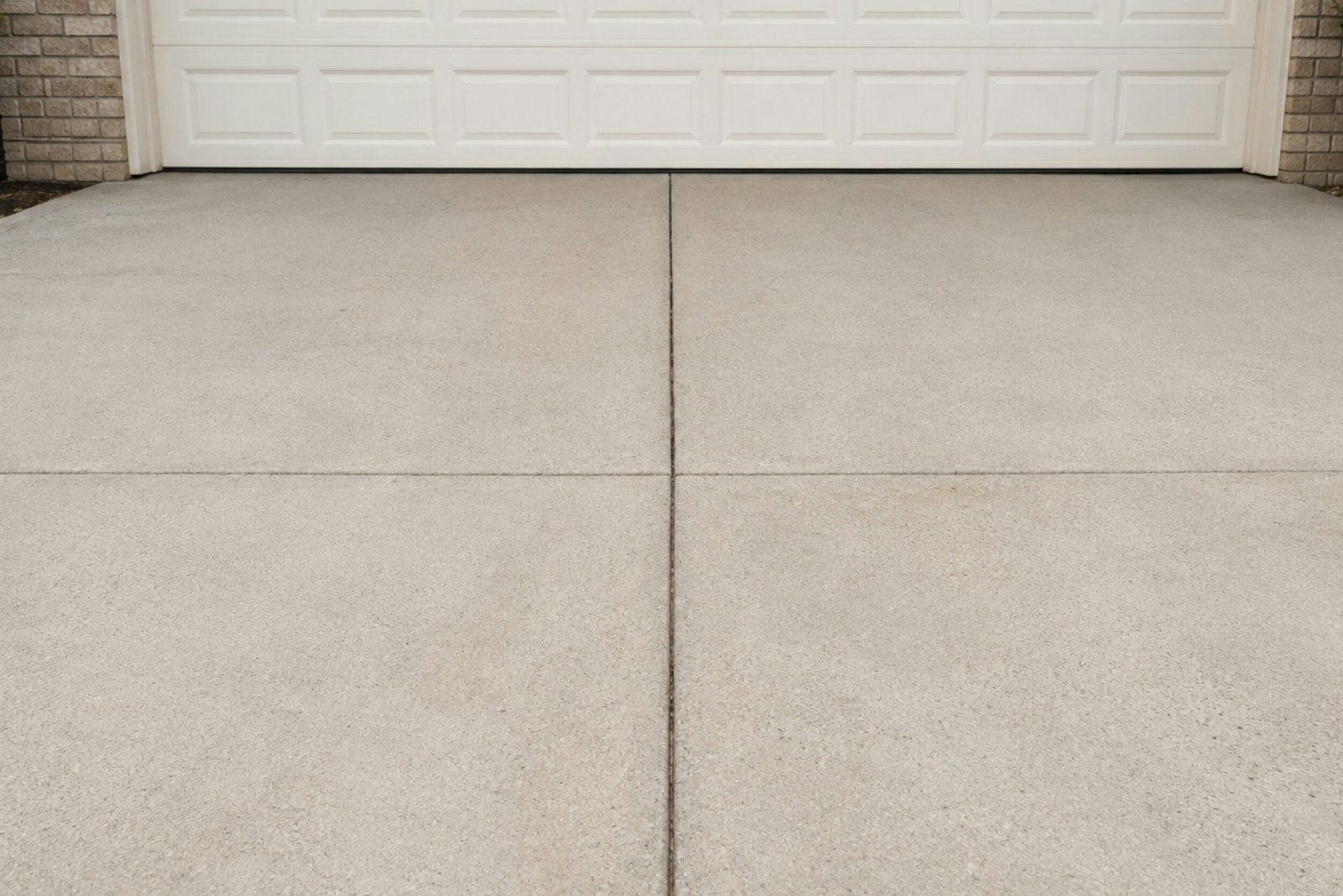 Clean residential concrete driveway with a saw-cut control joint leading to a home's garage — example of concrete driveway cost in Rochester, NH