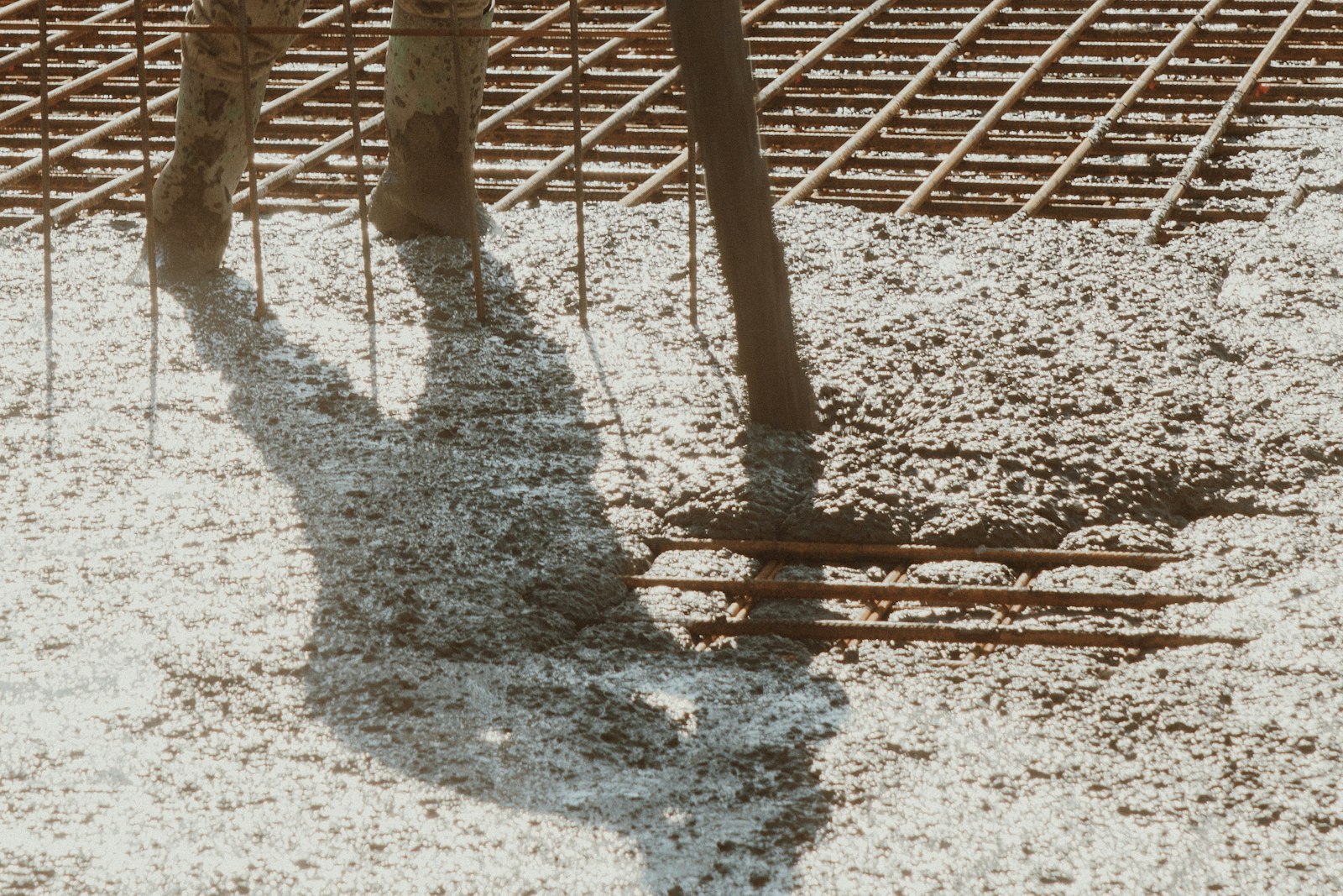 Fresh concrete being placed over a steel rebar mat and compacted base — the reinforcement and base that determine how long a slab lasts
