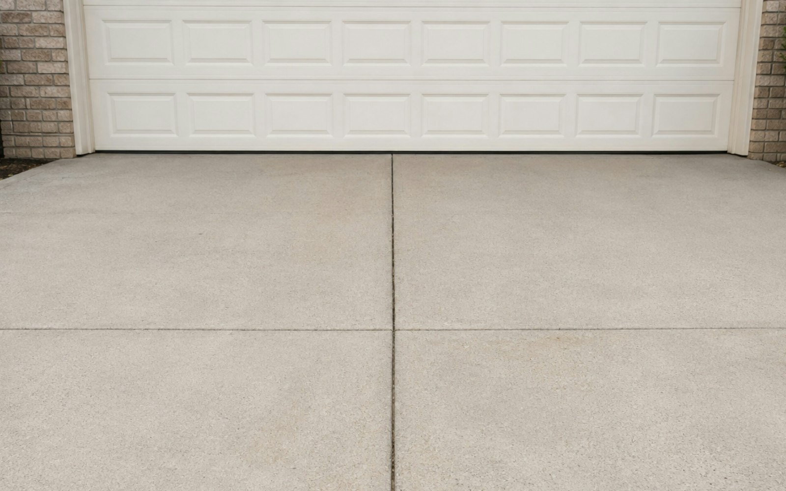 A clean, professionally finished concrete driveway with a straight saw-cut control joint in front of a home