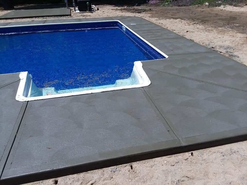 Wraparound concrete patio connecting a pool area with the backyard