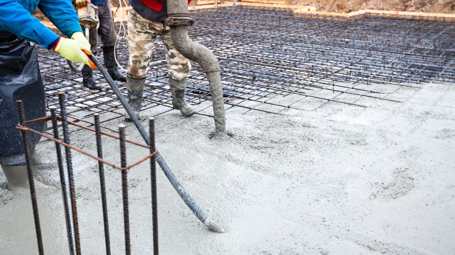 Construction workers pouring concrete over metal rebar reinforcement grid