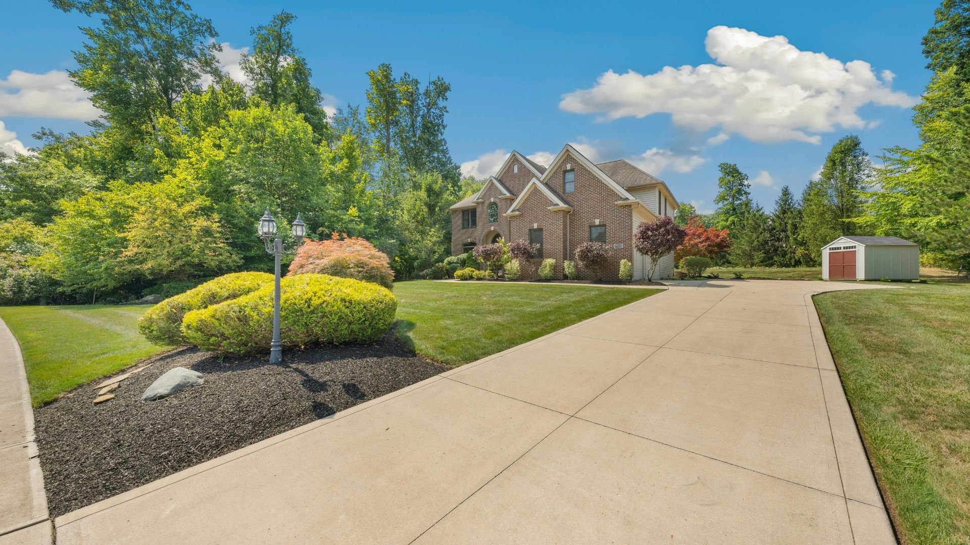 Brick house with manicured lawn, landscaped garden, and small shed on sunny day