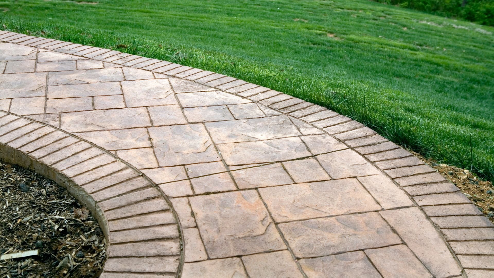Curved stone paver walkway with green grass and mulch border