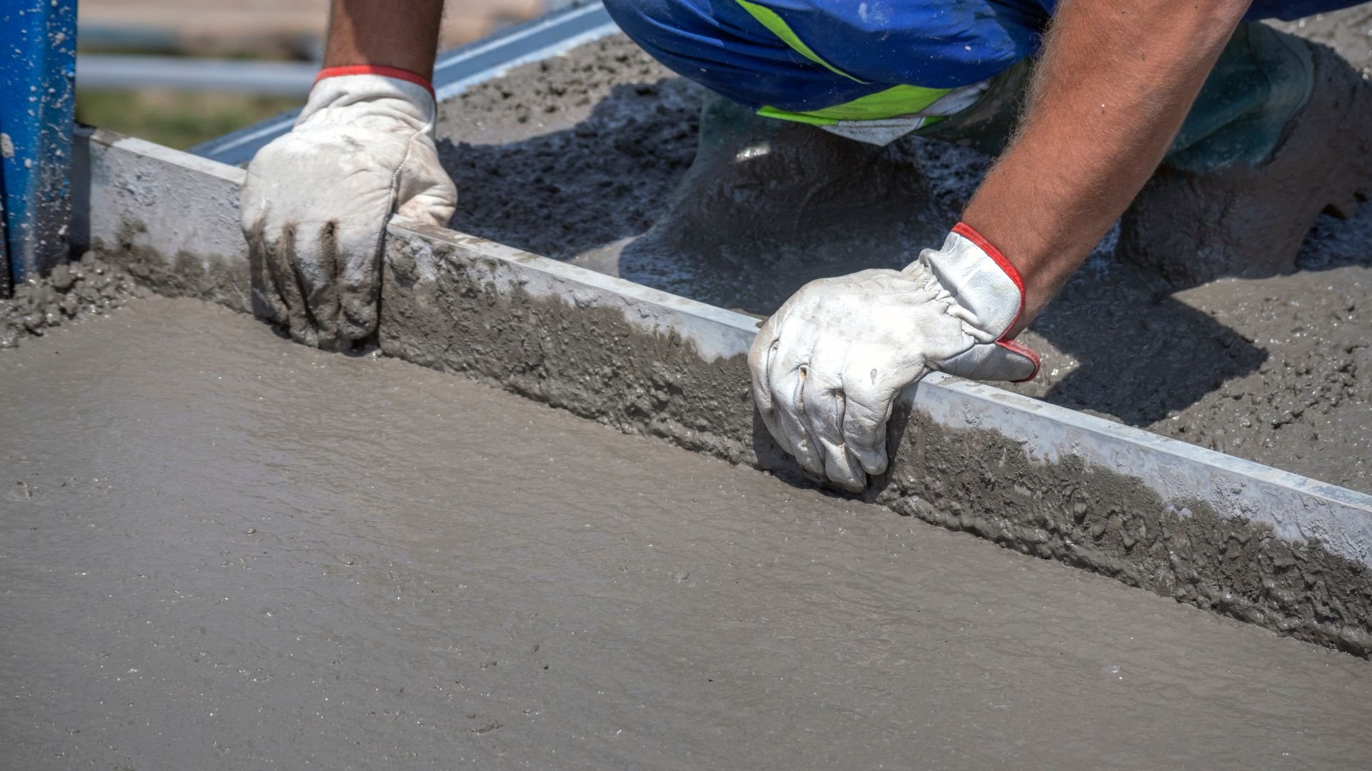 Construction worker smoothing wet concrete with leveling tool